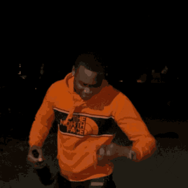 a man wearing an orange north face sweatshirt holds a bottle of wine
