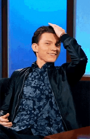 a man wearing a black jacket and a floral shirt is smiling and scratching his head