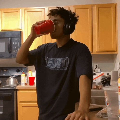a man wearing headphones drinking from a red cup in a kitchen