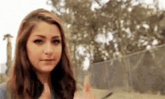 a young woman is giving a thumbs up in front of a fence and trees .