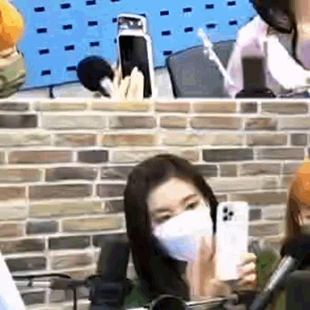 a woman wearing a mask is holding a cell phone in front of a microphone in a room .