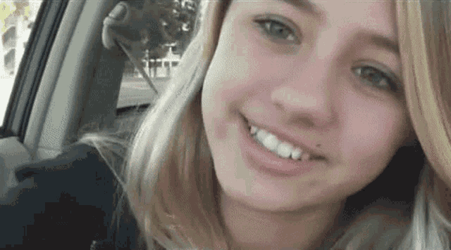 a young girl is sitting in the back seat of a car and smiling .