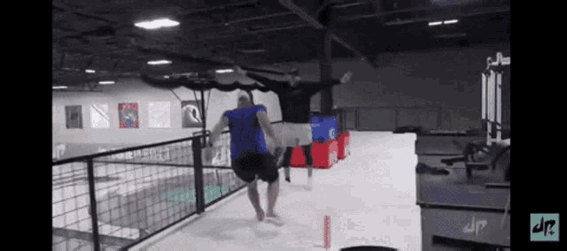 a man in a blue shirt jumps over a fence in a gym