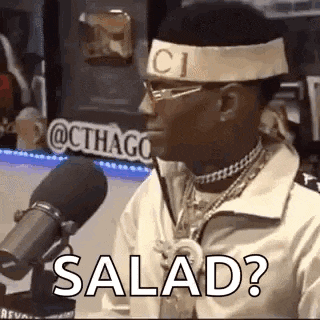 a man wearing a headband and glasses is sitting in front of a microphone and saying `` salad ? '' .