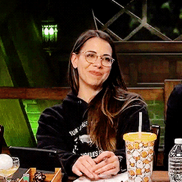 a woman wearing glasses is sitting at a table with a drink in front of her
