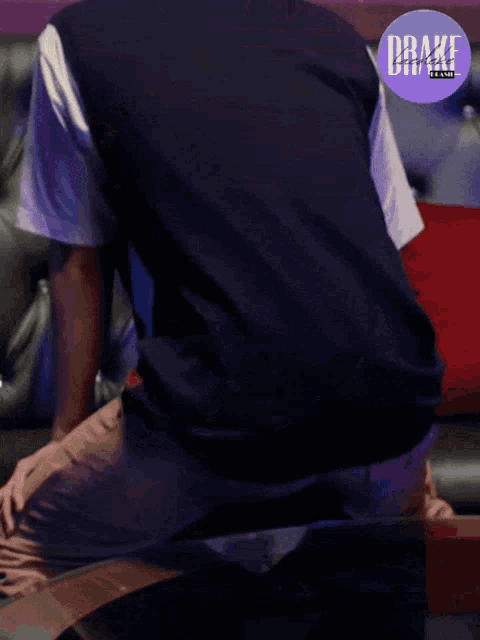 a man sitting on a couch with a drake band logo