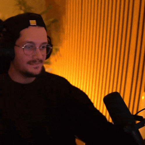 a man wearing glasses and headphones is sitting in front of a microphone with a yellow background