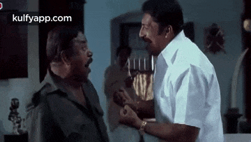 two men are standing next to each other in a room and talking .