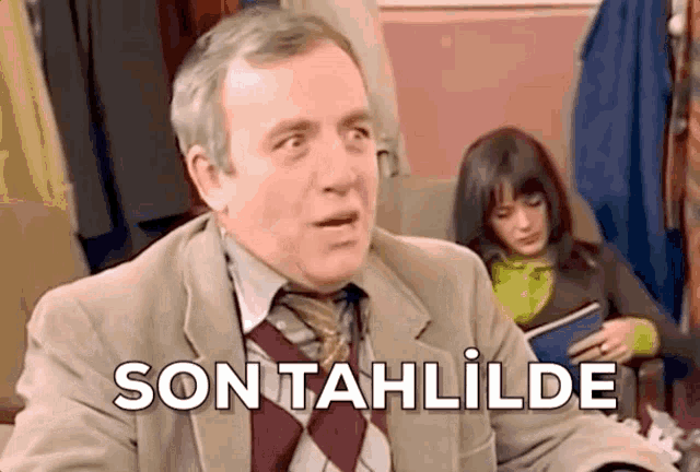 a man in a suit and tie is sitting in front of a woman holding a book and says son tahlilde .