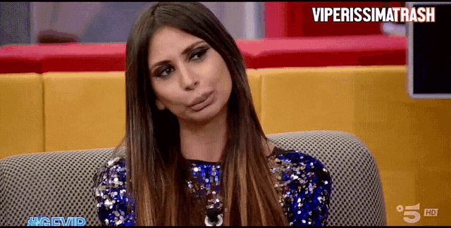 a woman in a blue sequined dress is sitting on a couch in front of a tv screen that says viperissimo trash