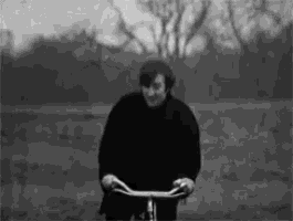 a man in a black jacket is riding a bicycle in a field .