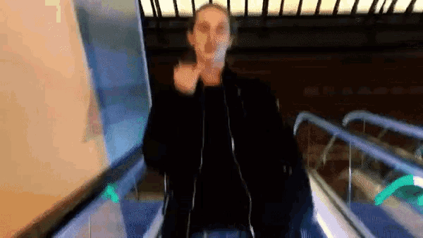a man in a black jacket is walking down an escalator and smoking a cigarette .