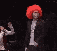 a man wearing a red afro wig is dancing on stage .