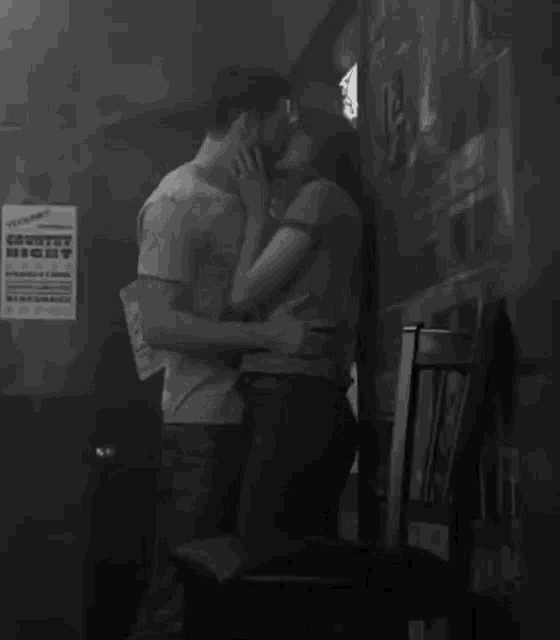 a black and white photo of a man and woman kissing in front of a poster that says ' country night ' on it