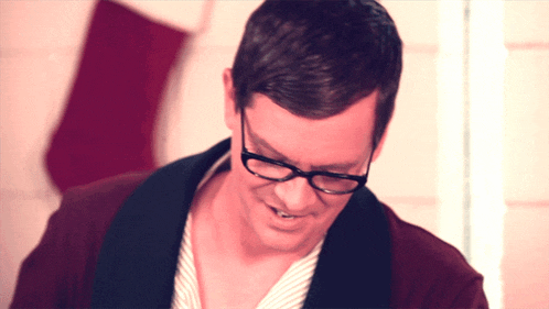 a man wearing glasses and a robe smiles in front of a christmas stocking