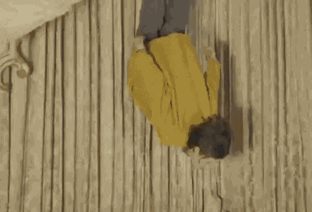 a man in a yellow jacket is doing a handstand upside down on a wooden floor .