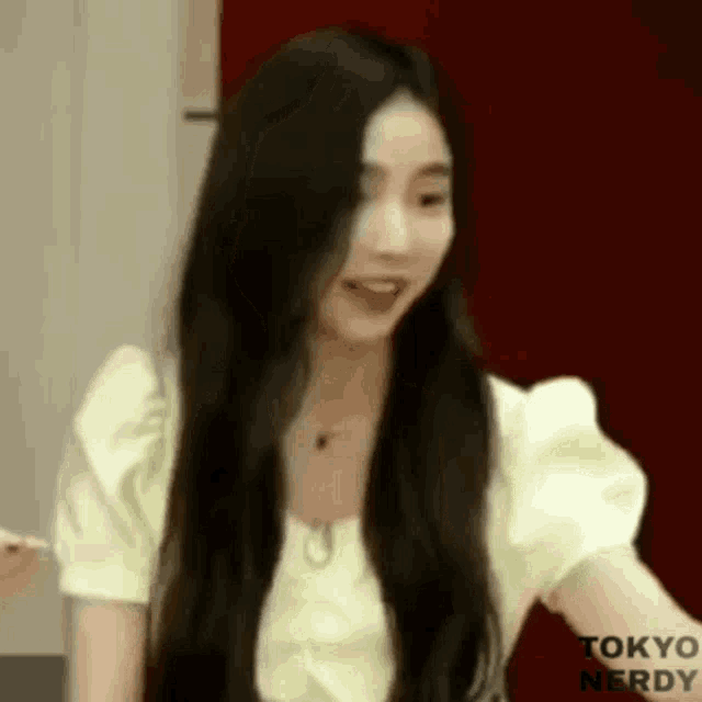 a woman with long black hair is wearing a yellow shirt and looking at the camera .