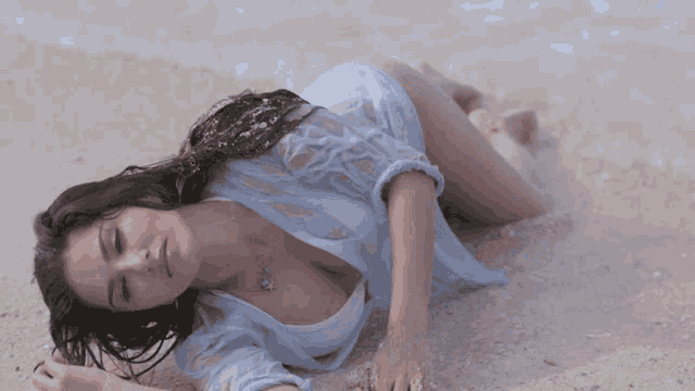 a woman in a blue shirt laying on the beach