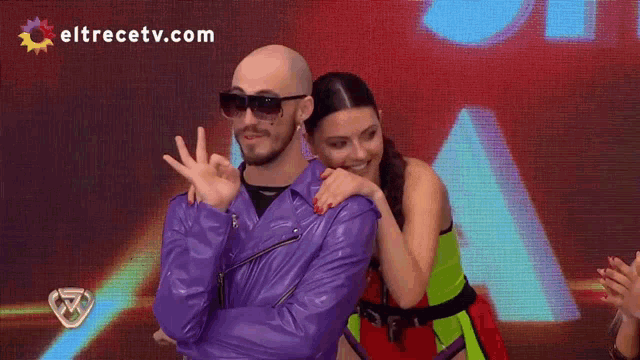 a man in a purple leather jacket is being hugged by a woman in a green dress