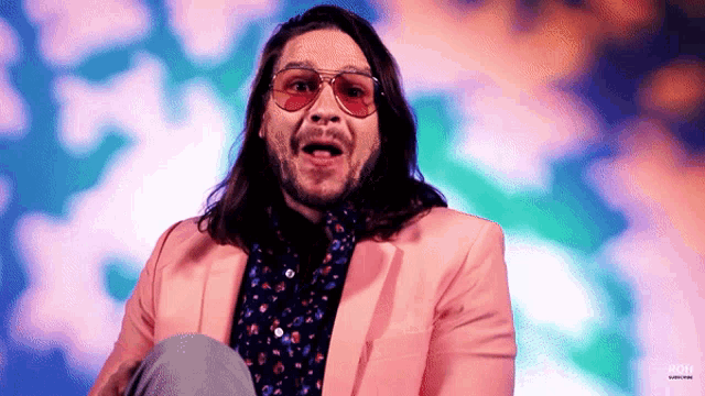 a man wearing sunglasses and a pink jacket is sitting on a stage