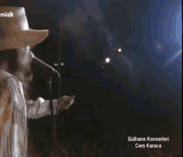 a man in a cowboy hat singing into a microphone with the words gülhane konserleri cem karaca in the corner