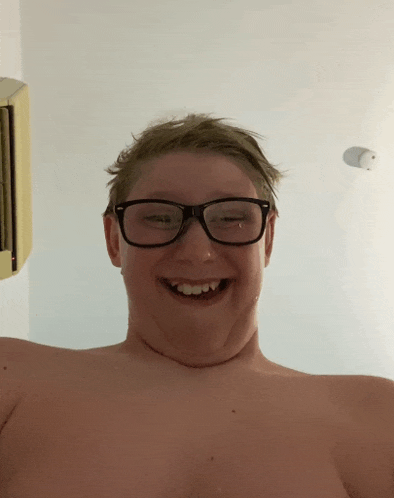 a shirtless young man wearing glasses is smiling
