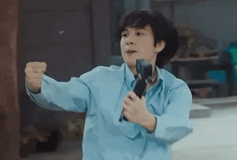 a young man in a blue shirt is holding a microphone in his hands .
