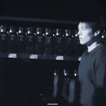 a black and white photo of a man standing in front of a shelf with bottles of wine on it