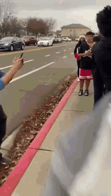 a group of people are standing on a sidewalk next to a road