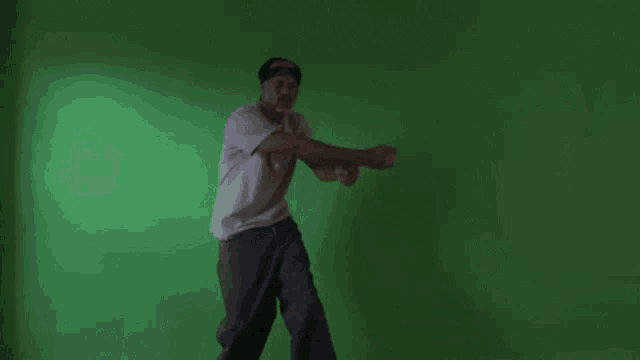 a man in a white shirt is dancing in front of a green wall