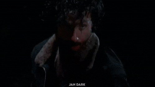 a close up of a man 's face in the dark with a beard and curly hair .