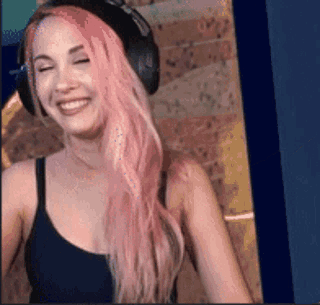 a woman with pink hair wearing headphones and a black tank top .