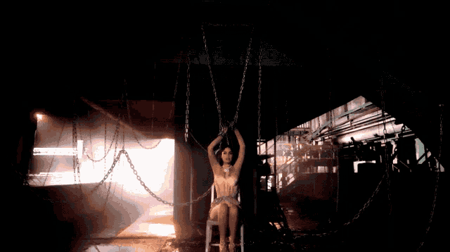 a woman is chained to a chair with chains hanging from the ceiling