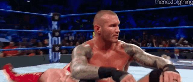two men are wrestling in a wrestling ring and one is laying on the ground .