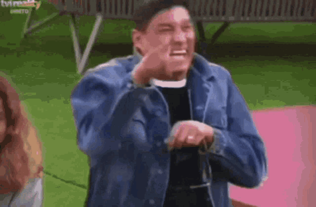 a man in a denim jacket is making a funny face while standing on a pink mat .