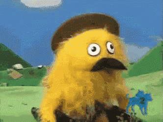 a yellow puppet with a hat and mustache is standing in a field