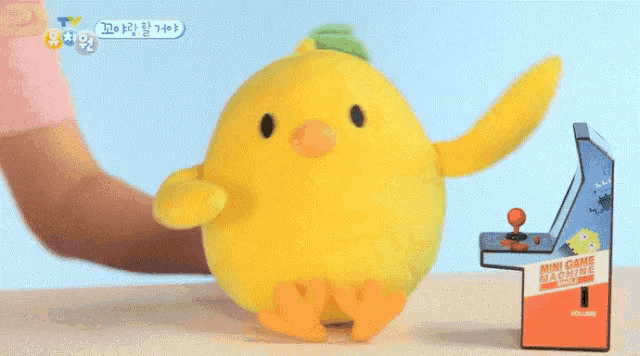 a stuffed yellow chicken is sitting next to a small mini game machine
