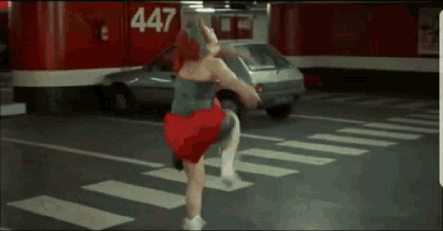 a woman in a red dress is crossing a street in front of a parking garage .