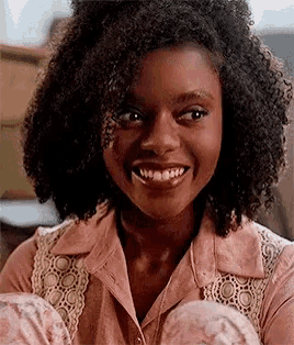 a young girl with curly hair is smiling while wearing a pink shirt and pajamas .