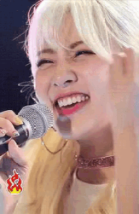 a woman with white hair is singing into a microphone while smiling .