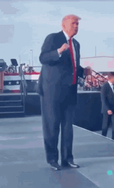 a man in a suit and tie is standing on a stage in front of an american flag