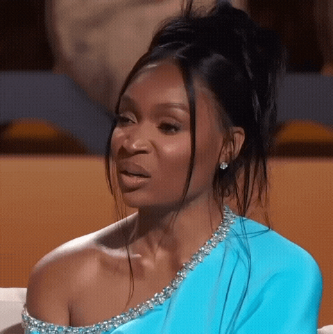 a woman in a blue dress is sitting on a couch and making a face .