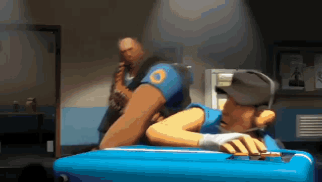 a man is laying on a blue suitcase while another man stands behind him