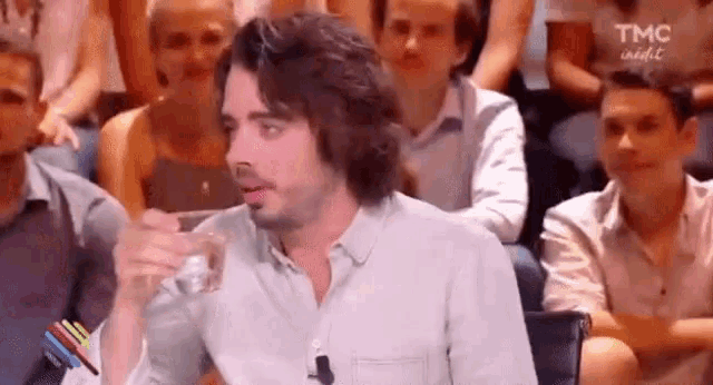 a man is holding a glass of water in front of a crowd .