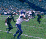 a football player is catching a ball on a field while another player tries to block him .