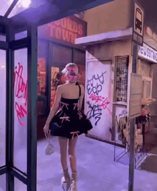 a woman in a black dress is walking through a bus stop at night .