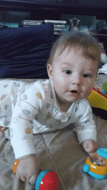 a baby is crawling on a bed playing with a toy car