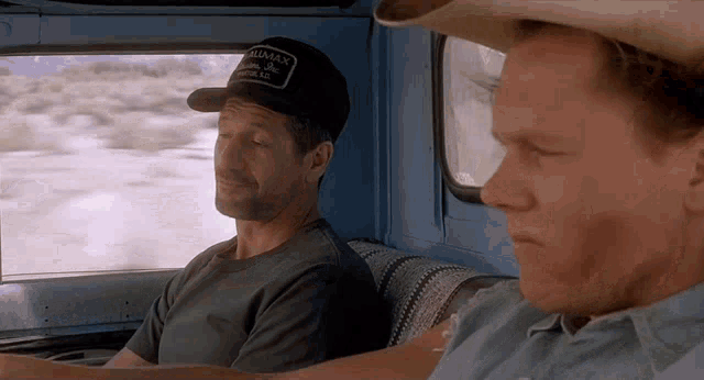 a man wearing a hat that says alaska on it sits next to another man