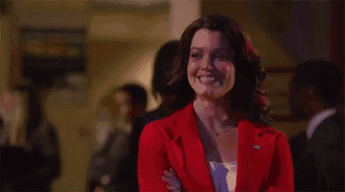 a woman in a red suit is smiling with her arms crossed in a room .