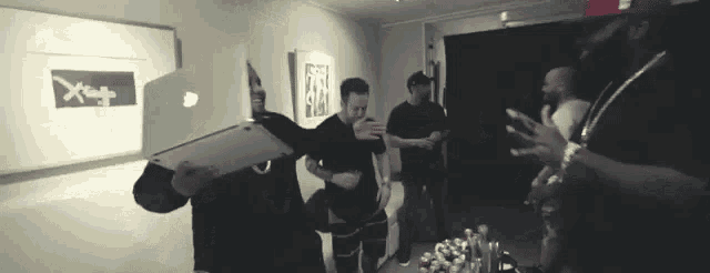 a group of men are standing in a room and one of them is holding an apple laptop in front of his face .